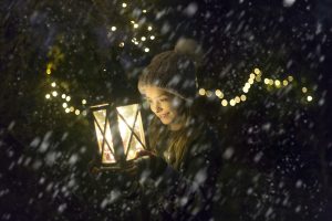 Happy girl with lighted lantern by night at snowfall